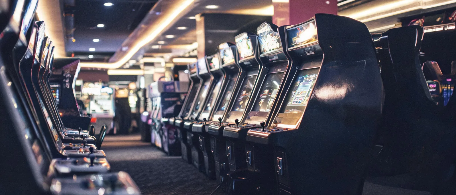 娛樂城電子遊戲區走道兩側並列的直立式遊戲機台,面板亮著柔和的光